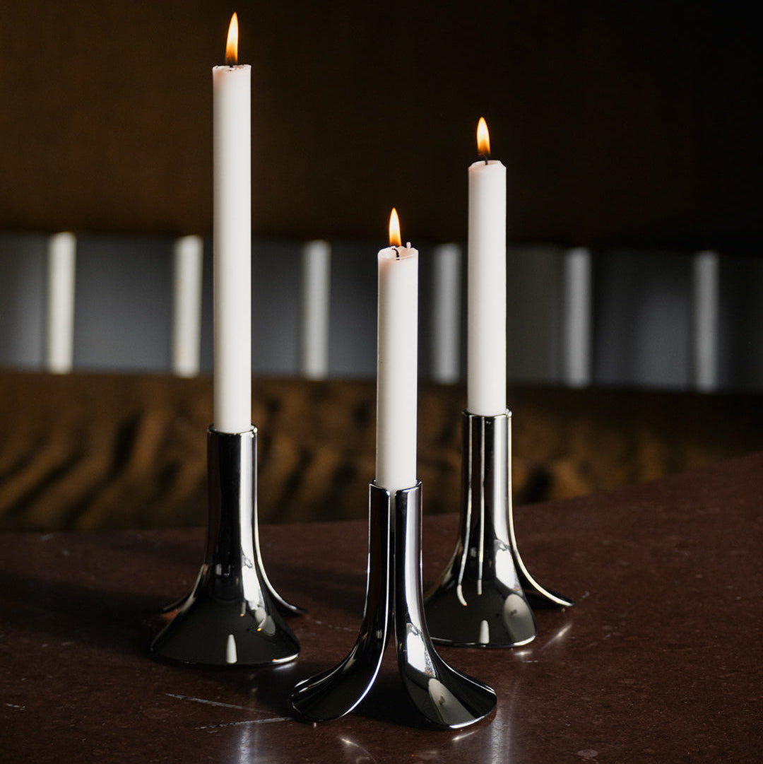 Three lit candles in black holders on a wooden surface with a blurred background